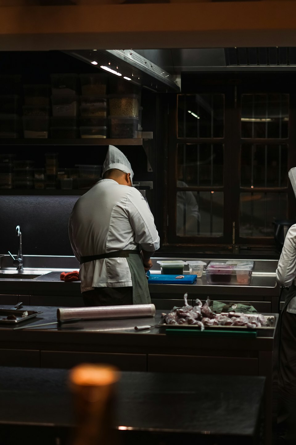 Chef con uniforme blanco prepara comida en una cocina concurrida.
